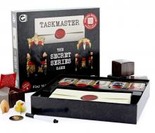 Taskmaster Boardgame box with Greg Davies on the front, with contents on a white background showing task envelopes, markets and game pieces 
